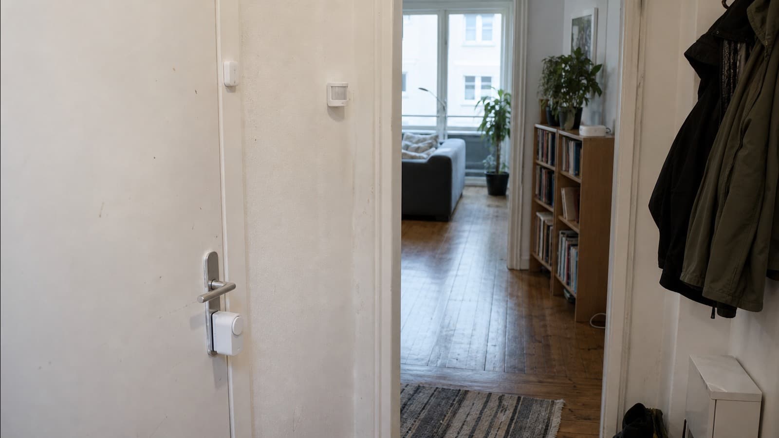 Smart lock and sensors installed in the entrance area of a lived-in apartment, with a small home hub on a bookshelf