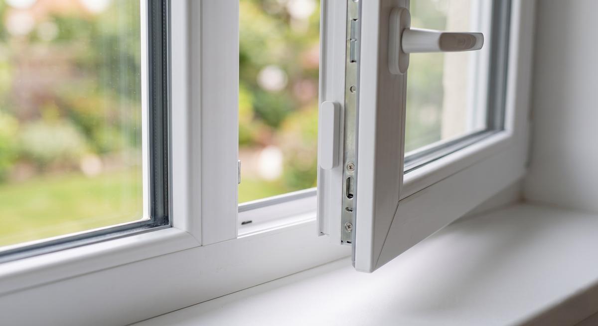 Hand klebt einen weißen Funk-Fensterkontakt mit Klebepad an einen weißen Kunststoffrahmen